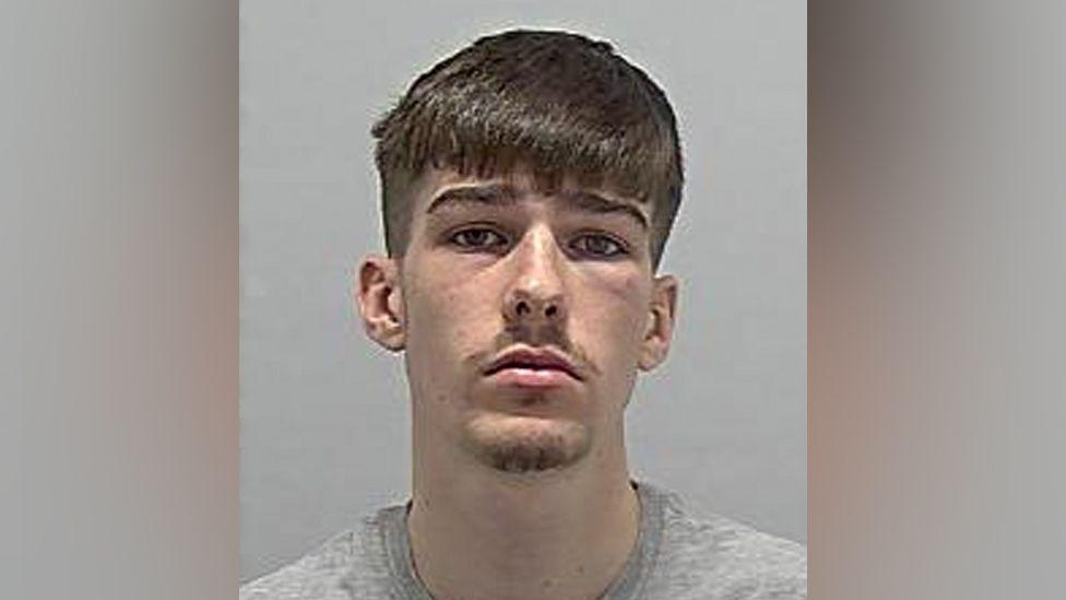 A police mugshot of Jacob Zuco, who has brown hair that is cut just above his eyebrows. He has stubble and a serious look on his face.
