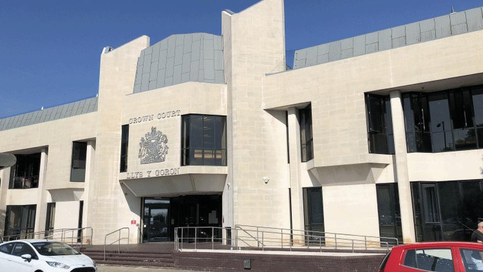 The white stone frontage of Swansea Crown Court. In front of the building are some brick steps, metal railings and parked cars