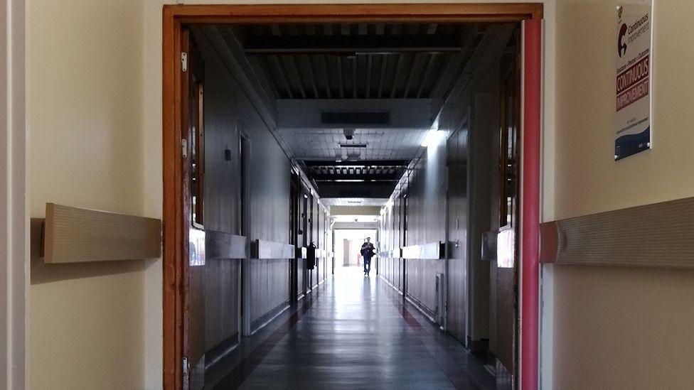 An internal corridor narrowing into the distance at Royal Preston Hospital. It is dark and unlit and there is a person in the distance