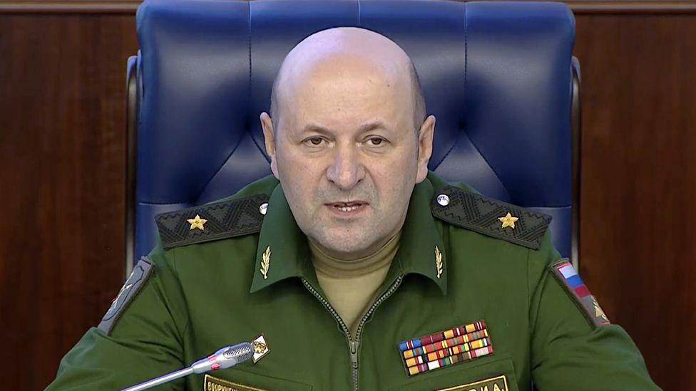 Igor Kirillov, who has a bald head and wears green military overalls, speaks into a mic during a press conference