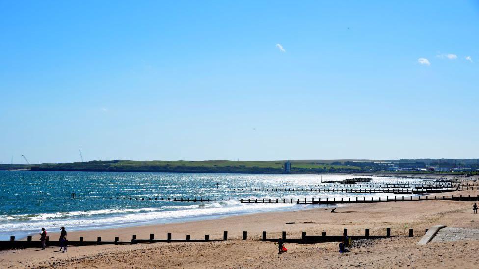 Sandy beach with wooden spines, blue sea and blue sky, in Aberdeen