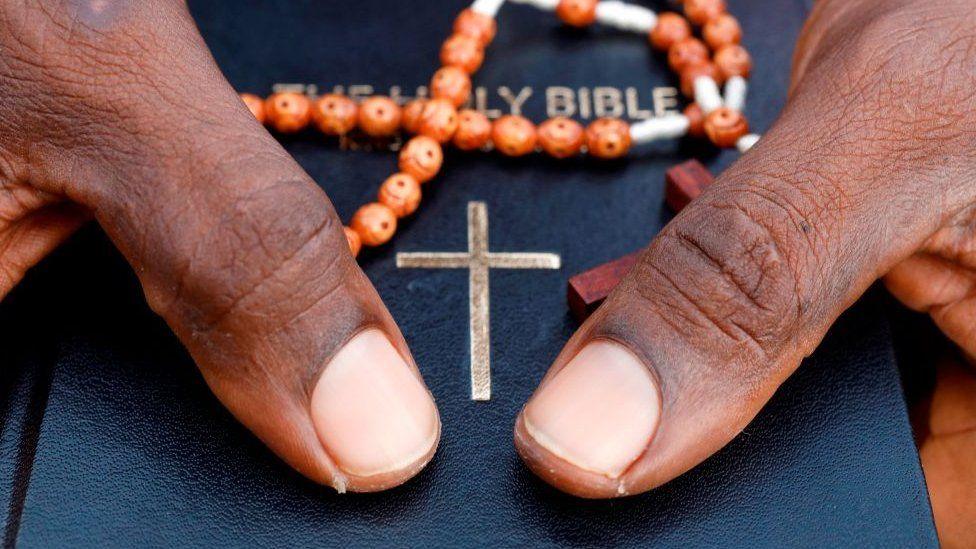 Close-up of hands holding a bible and orange prayer beads