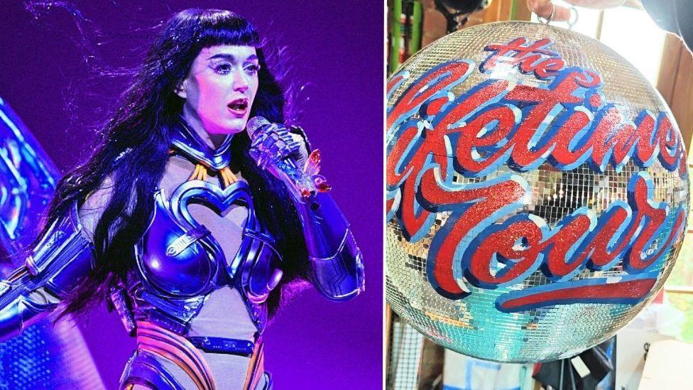 A picture of Katy Perry, a singer with long dark hair and a fringe performing on stage in a costime which lokos a bit like a robot. She is singing into a microphone. On the other side is a mirrorball with the words 'The Lifetimes Tour' painted on. 
