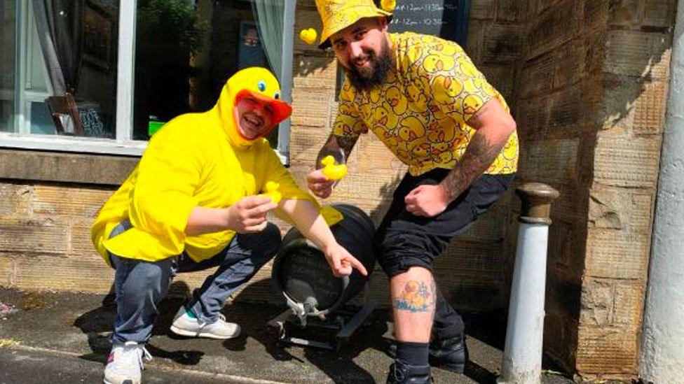 Daniel Caldwell and Curtis Lunt in their duck outfits showing Curtis's yellow rubber duck tattoo on his left calf