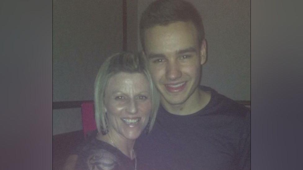 Kerri has blonde short hair and is wearing a black top. She is smiling with Liam Payne who has short brown hair and a black long sleeved top