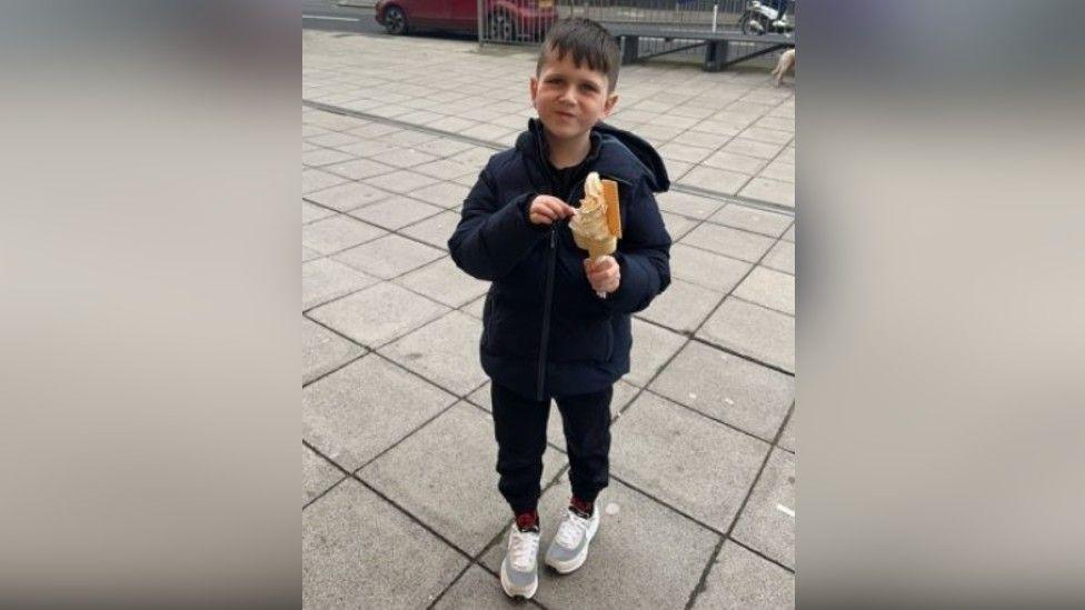 Archie holding an ice cream. He wears a dark coloured coat.