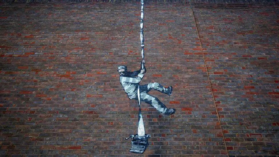 Artwork, created by Banksy, of a prisoner climbing down the prison wall using a typewriter 