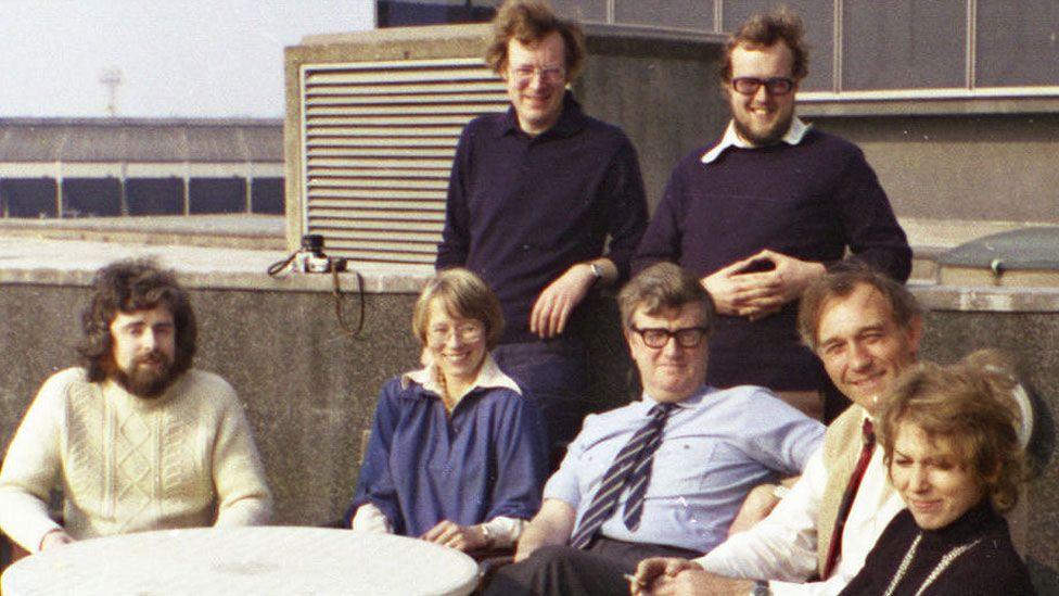 Two standing men are Ian Irving (left) and Ian Morton-Smith (right) and seated from left are Adrian Robson, Linda Alexander, Colin McIntyre (Editor), Peter Wheadon and Rita Carter, on the roof of BBC Television Centre in the 1970s