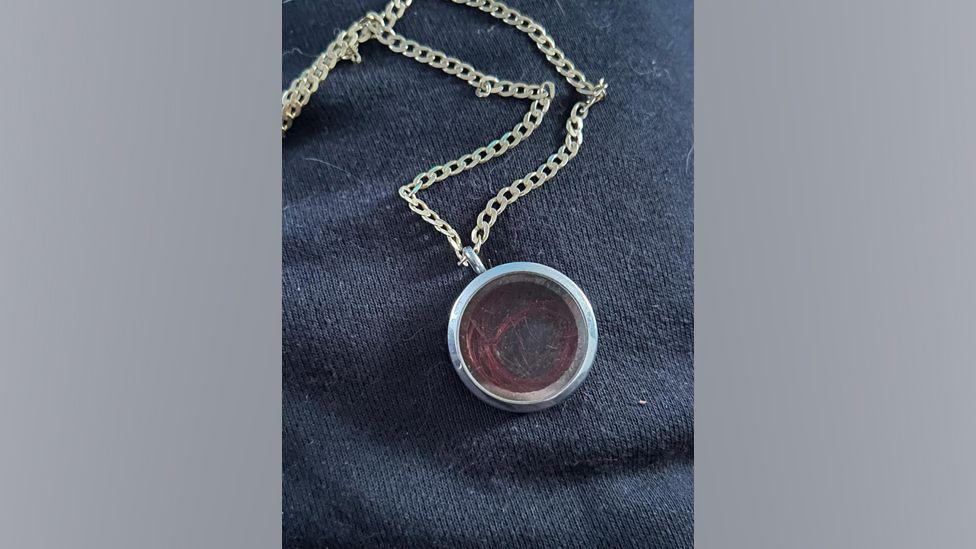 The locket containing Taylor Black's hair. The hair is contained within glass in a silver circular locket. It is attached to a silver chain.