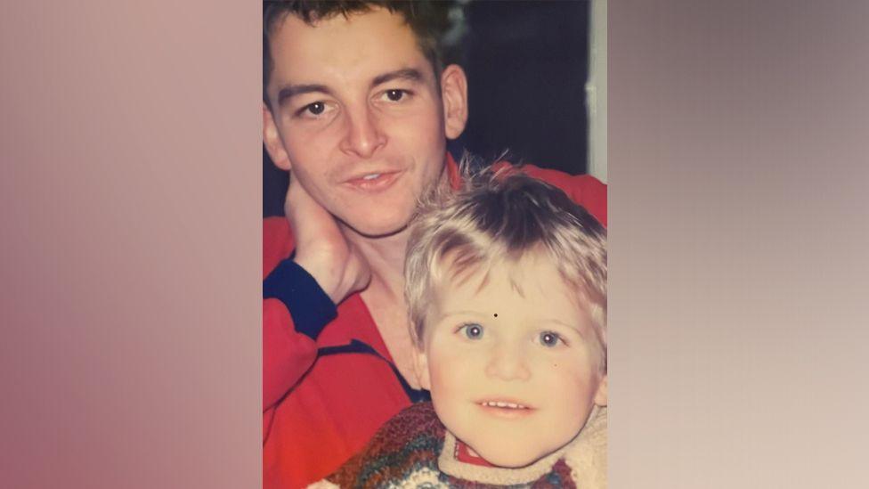 An old family photograph of Fred resting his head on his hand with a young Jack in his lap