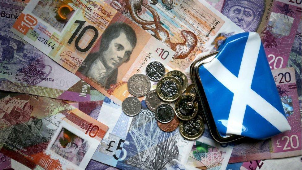 A pile of Scottish banknote and coins next to a saltire coin purse