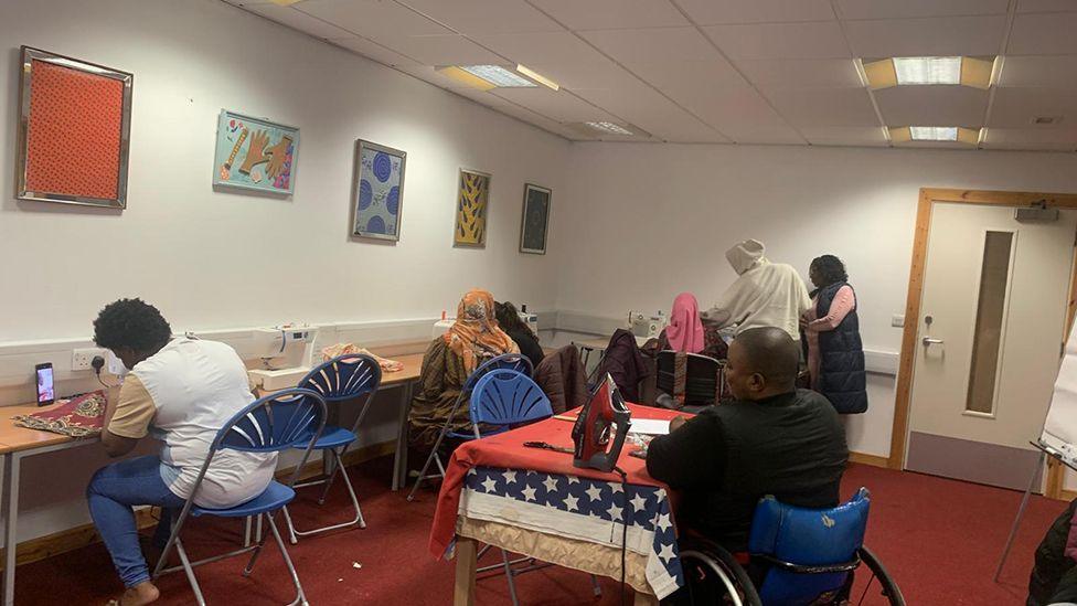 A group of people with their backs to the camera taking part in a sewing class at the refugee centre