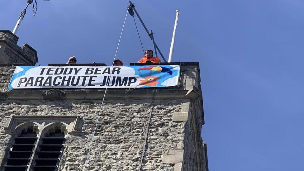 A sign that reads "teddy bear parachute jump" on the top of the church tower