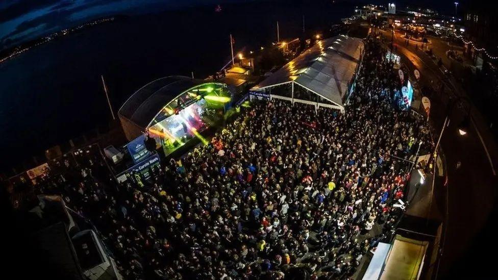 An arial view of the Bushy's tent at the Bottleneck car park. It is full of people. There is a tent with a stage and musicians on the left, with another tent at the back.