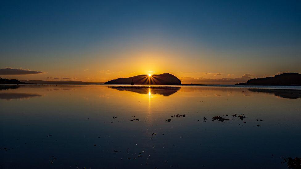 Sunrise over an island in a loch, golden and blue shades in sky.