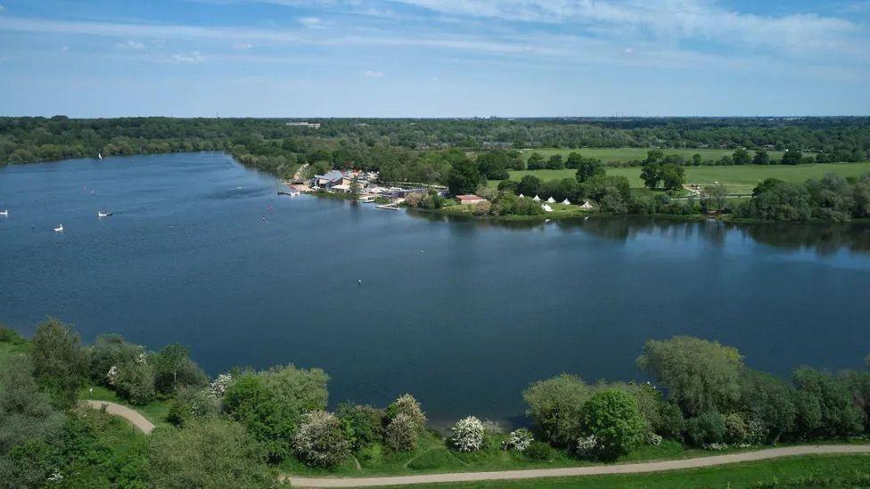 A wide expanse of lake can be seen from a bird's eye view, with trees, fields and a small number of buildings on either side. 