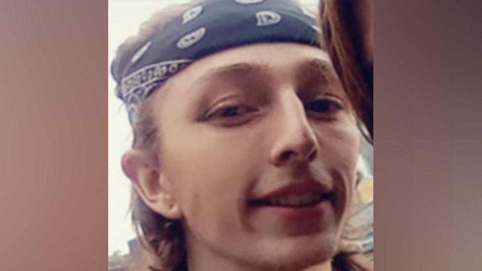 Jacob Clark with shoulder-length hair. He is wearing a blue and white bandana around his forehead