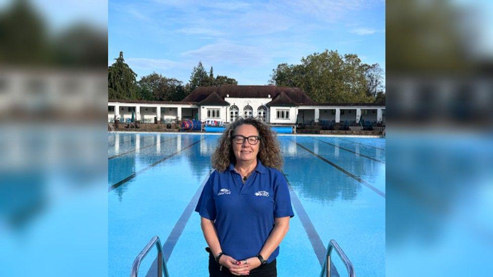 Julie in her uniform blue polo shirt standing on the poolside with the Lido behind her and the cafe in the background