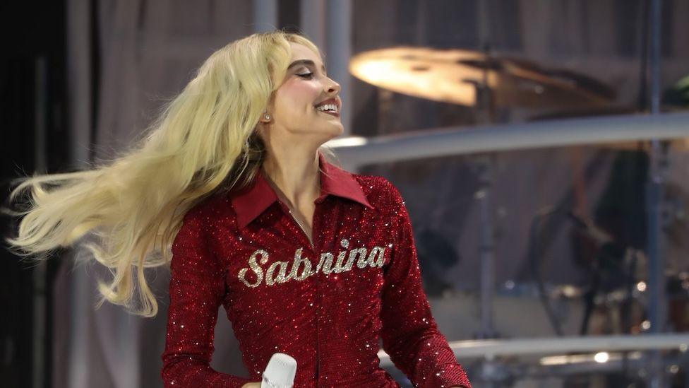 Sabrina Carpenter in an red top with her name in gold writing