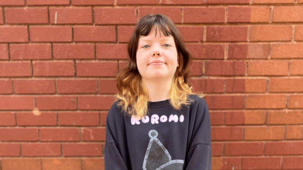 A young woman stands in front of a brick wall