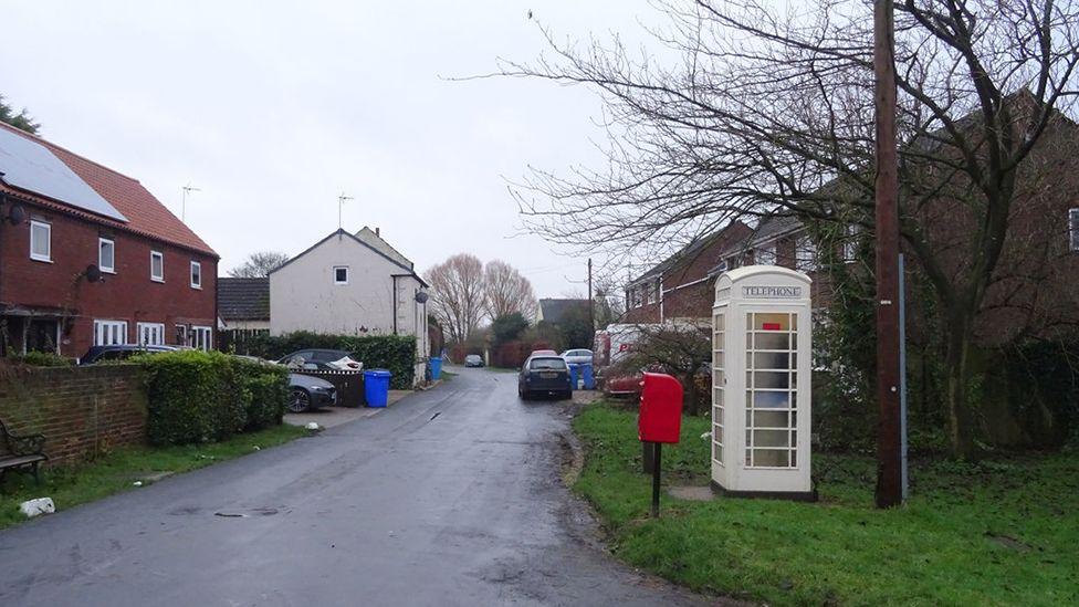 View of houses in Carr Lane in Weel with cars parked on drives and a cream phone box and red post box in the foreground