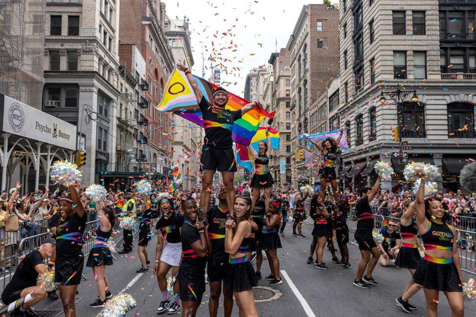 New Yorkers celebrate during the annual Pride March into the West Village on June 30, 2024 in New York City.  The images shows cheer leaders performing with sparkling pom poms while walking down a street with New York city skyline in the background