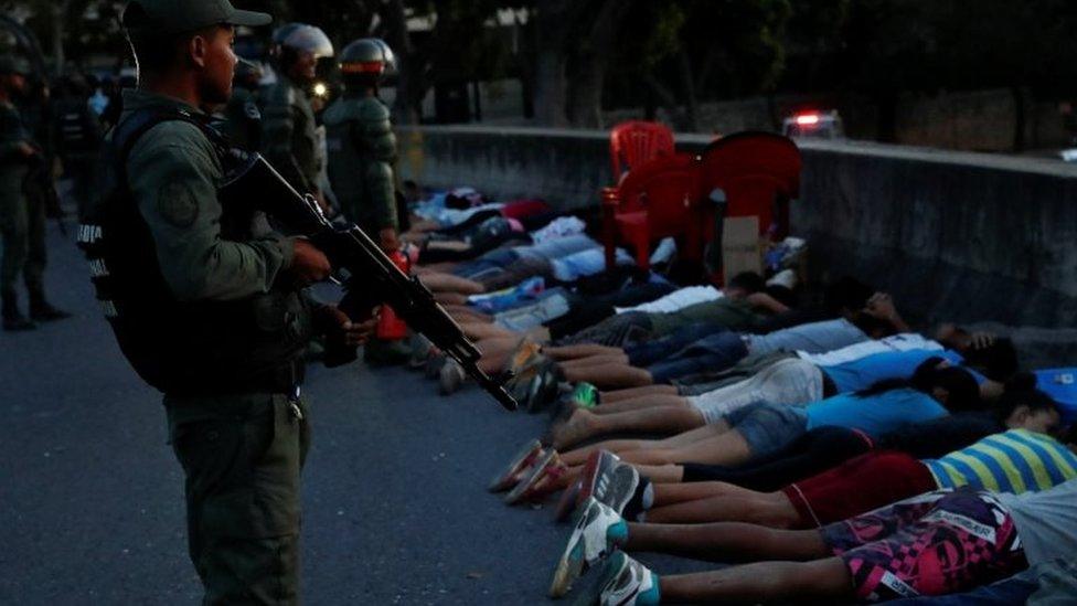 A security force member stands next to detainees on a street after looting during an ongoing blackout in Caracas, Venezuela March 10, 2019