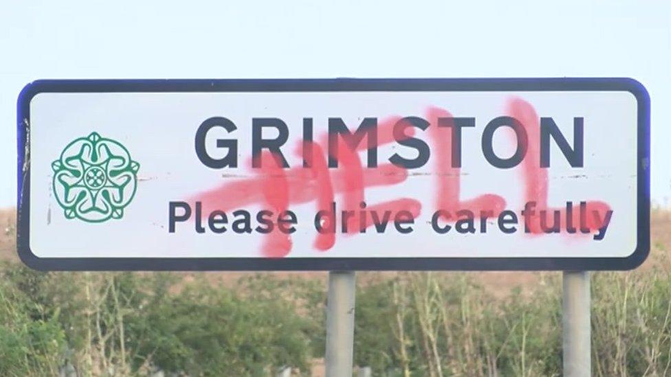 Grimston village sign with the word "hell" graphitised across the plaque