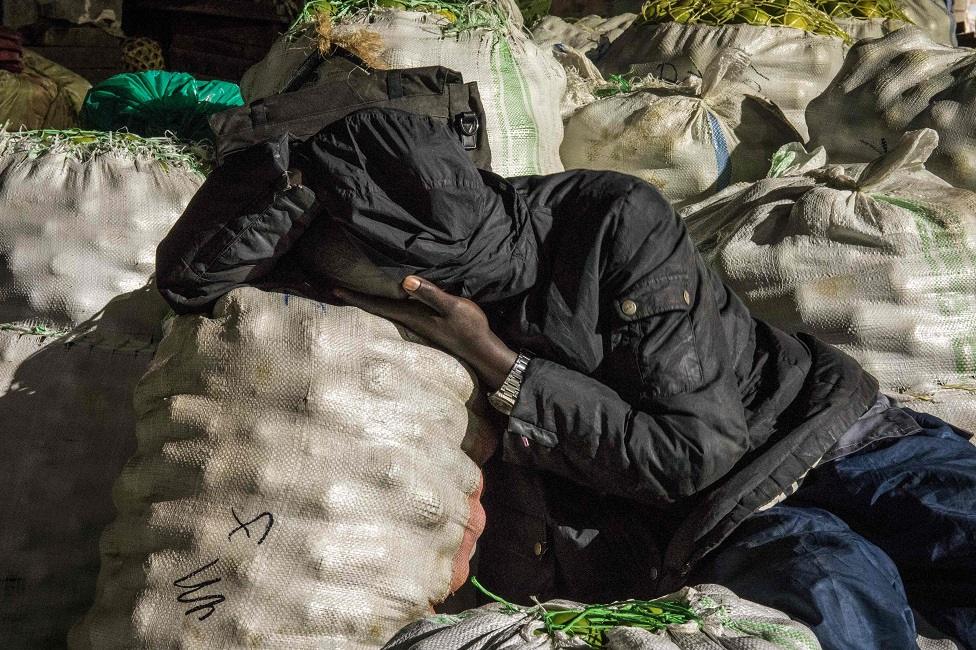 A trader sleeps next to items to be sold at a market following a directive from Ugandan President Yoweri Museveni that all vendors should sleep in markets for 14 days