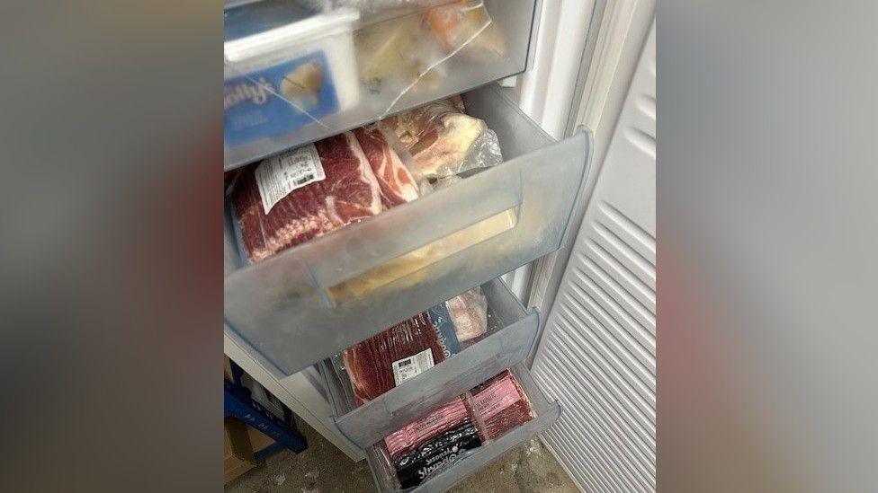 The inside of a freezer where the drawers have been pulled out and meat can be seen inside of it.