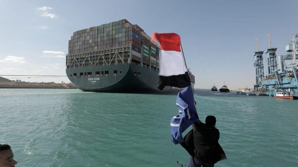 A man waves an Egyptian flag after the Ever Given is fully refloated in the Suez Canal, Egypt (29 March 2021)