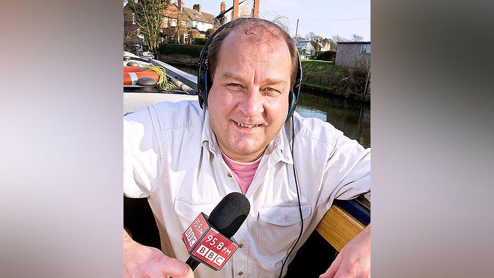 Andy Ball holding a BBC microphone aboard a canal boat from Runcorn to Liverpool on a sunny day