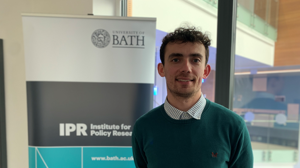 Man in green jumper stood in front of a University of Bath sign