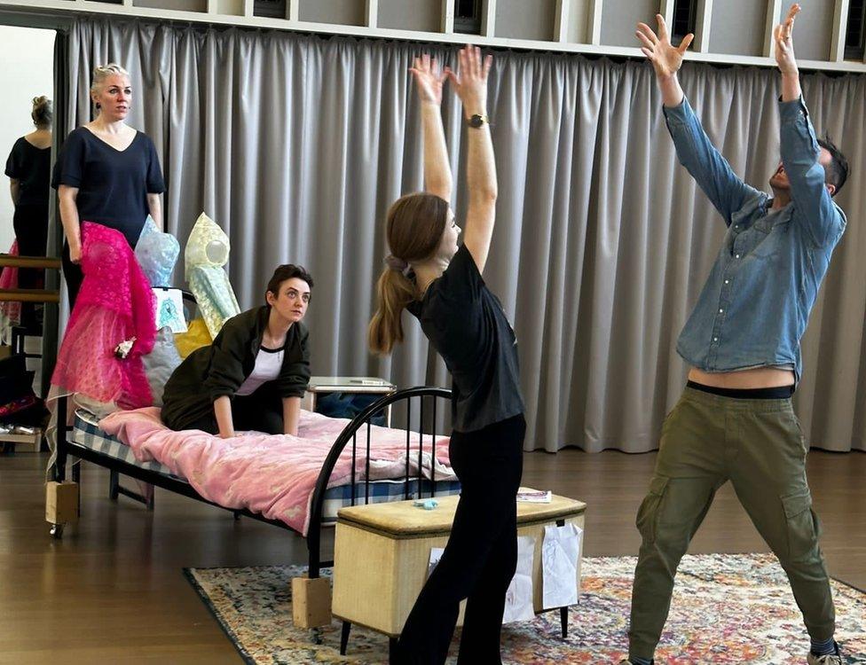 Cre8 actors rehearsing their play, Sleeping Beauty, ahead of the festival - woman on bed, woman stood beside her and male and female actors in front throwing books in the air