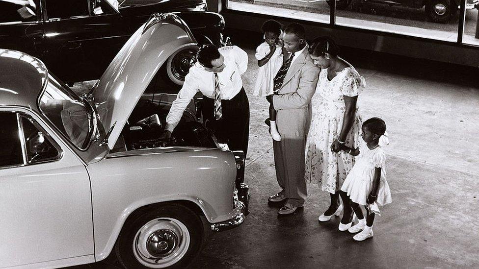 A family in Guyana are shown a Morris car in a showroom, 1958.