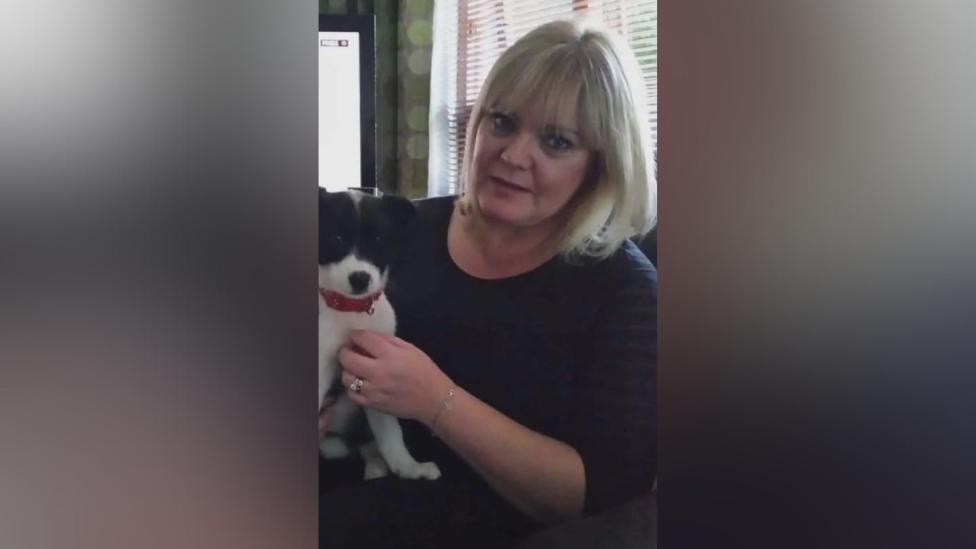 Louise with blonde hair and a blue top holding a dog