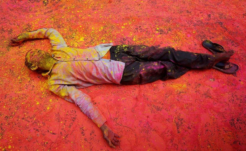 A Hindu devotee, smeared in coloured powder, takes a rest on a road during a procession for Holi celebrations in Kolkata