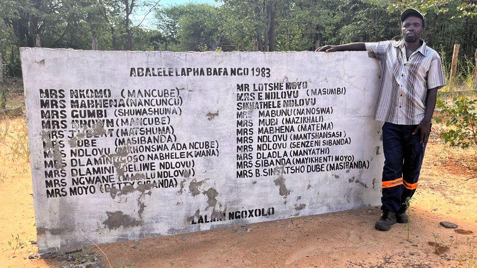 Thabani Dhlamini by a memorial wall to those who were killed in his village of Salankomo by Zimbabwean soldiers in 1983