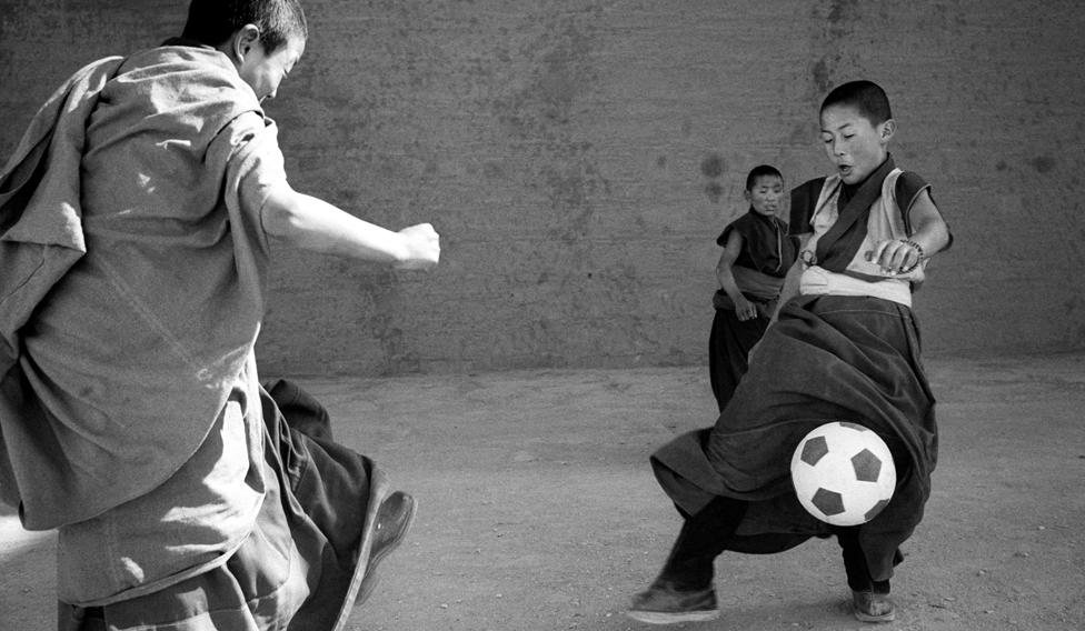 Two young monks play football while a third watches