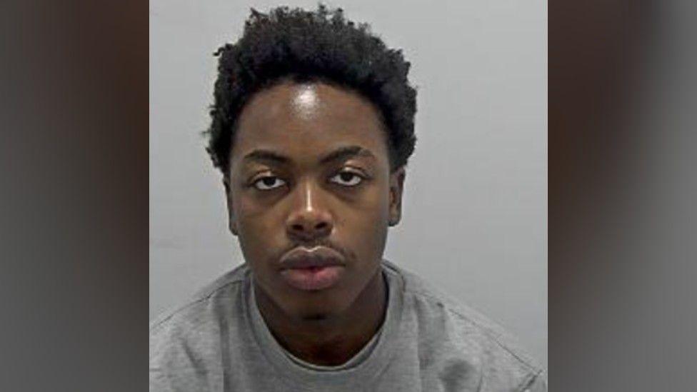 Bennett Ndenkeh: The head and shoulders of a man with black hair wearing a grey. round-necked top.