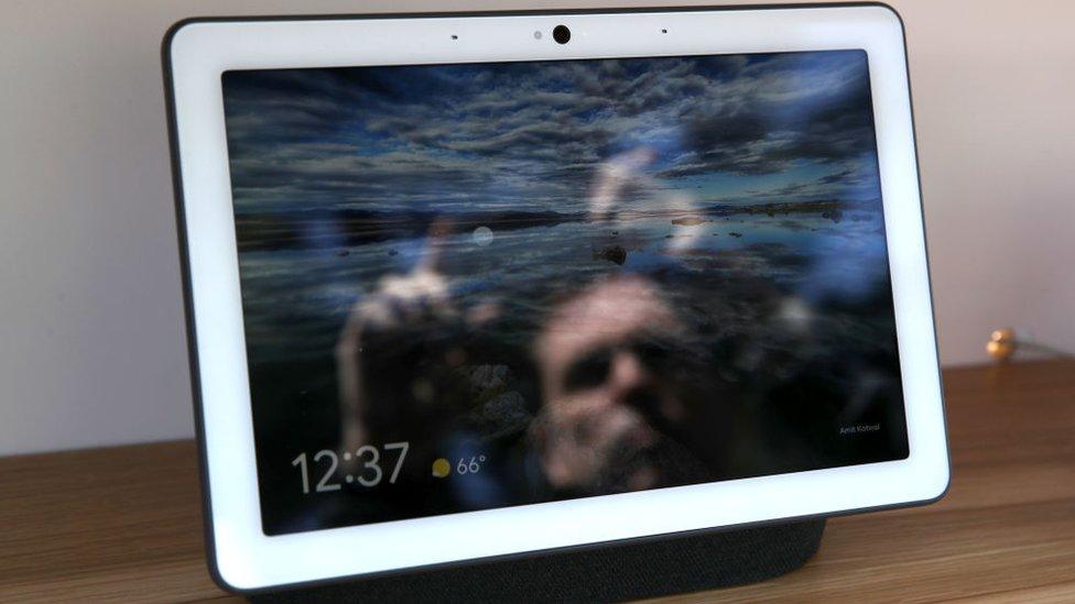 The reflection of a man is seen in a photo-frame style Google Nest Hub Max