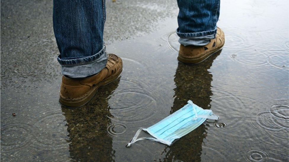 A man walks by a discarded face mask lying in a puddle