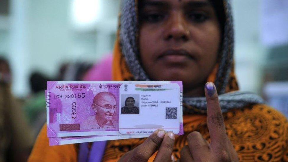 An Indian woman poses with new 2000 rupee notes, her Aadhaar ID card and a finger inked with indelible ink after exchanging withdrawn 500 and 1000 rupee banknotes at a bank in Chennai on November 17, 2016