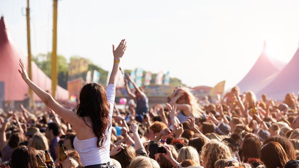 Young woman in a crowd with her hands in the air at a music festival.