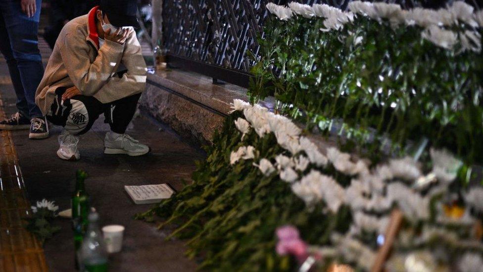 A man squats beside one of the many Itaewon memorials, set up overnight, and covers his mouth with his hand