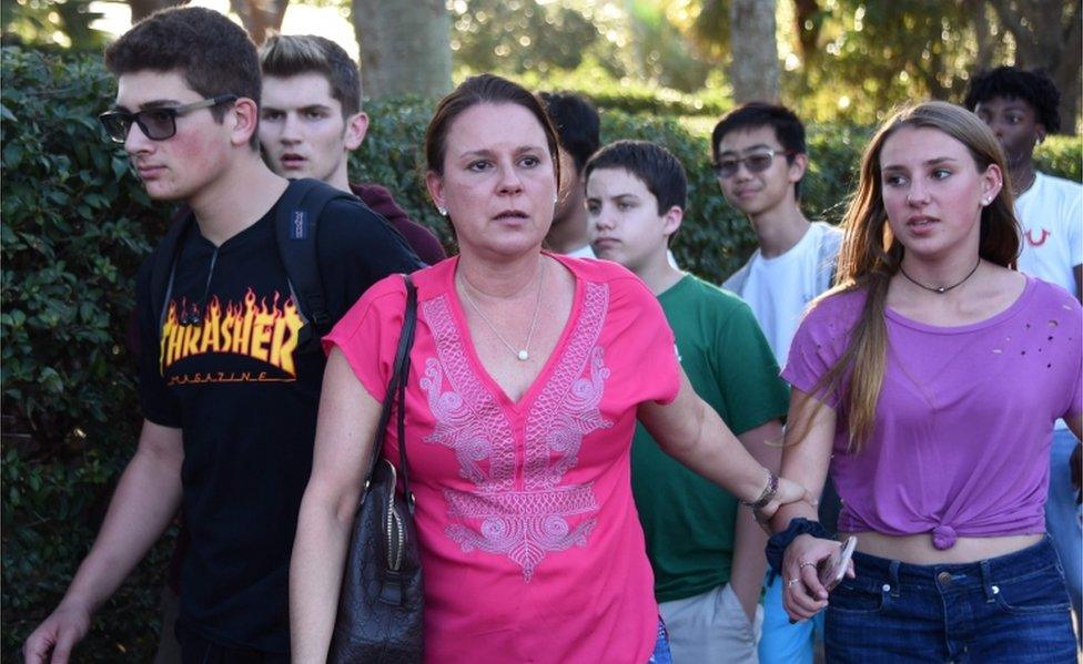 Students and adults holding hands leave the scene of Marjory Stoneman Douglas High School.