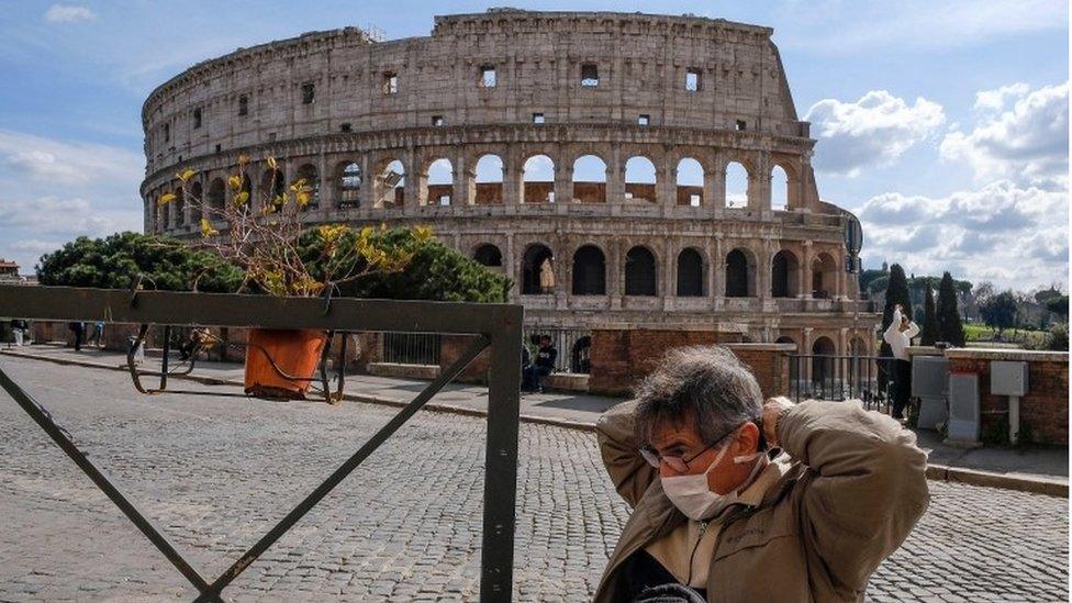 A tourist wearing a mask sits at the tables of a restaurant in front of the Coliseum, in Rome, Italy, 9 March 2020.