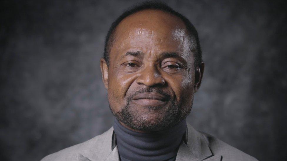 Head shot of Agomoh Paul from BBC interview, wearing grey polo neck and jacket