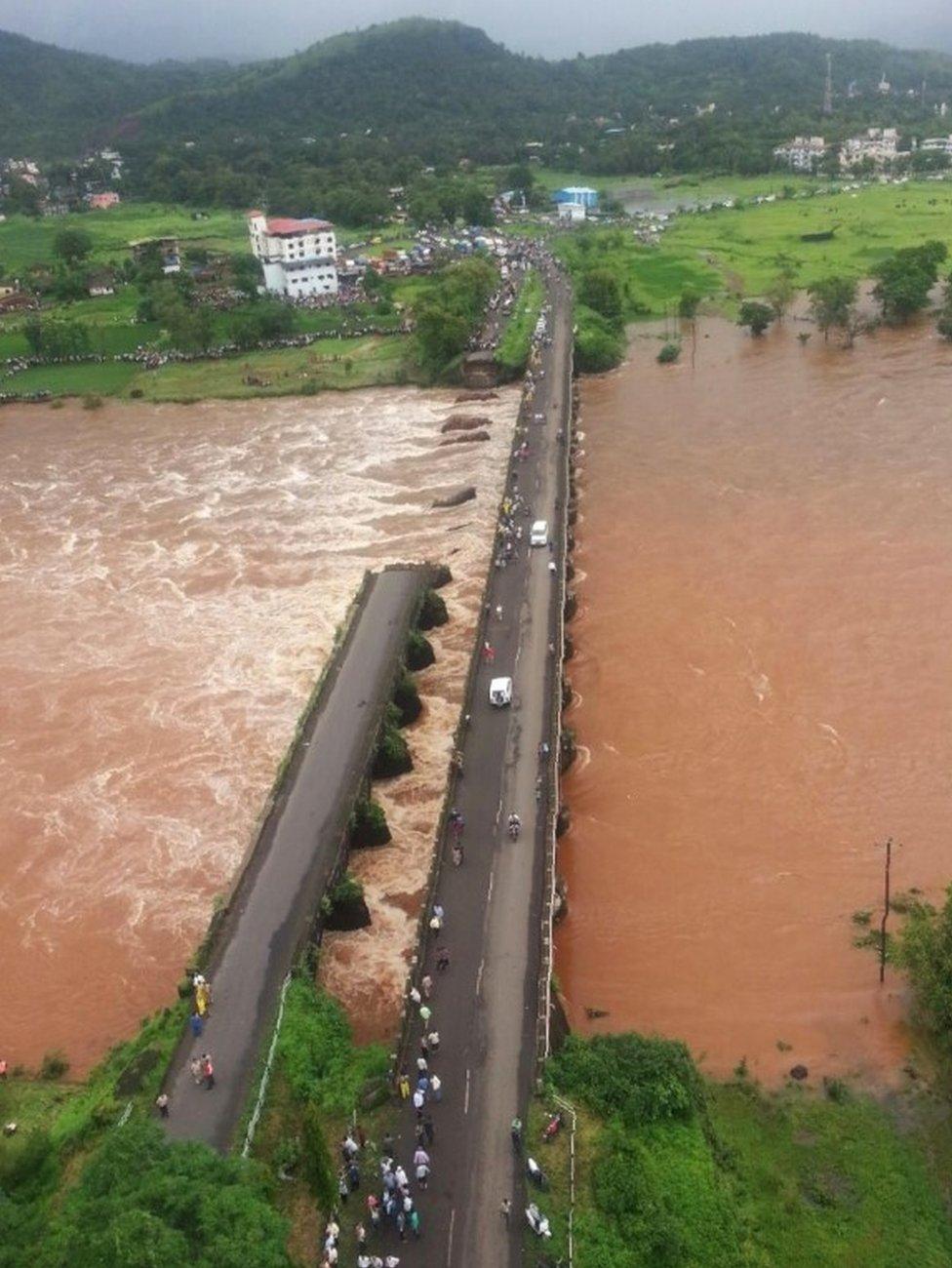 In this photograph released by The Indian Coastguard on August 3, 2016, Indian bystanders look at the wreckage of a partially collapsed bridge over the River Savitri in Raigad District some 100kms wouth of Mumbai