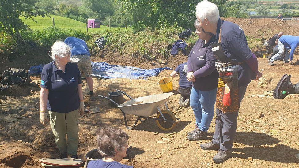 Three women and one man surrounded by mud and holes at an excavation at Irchester